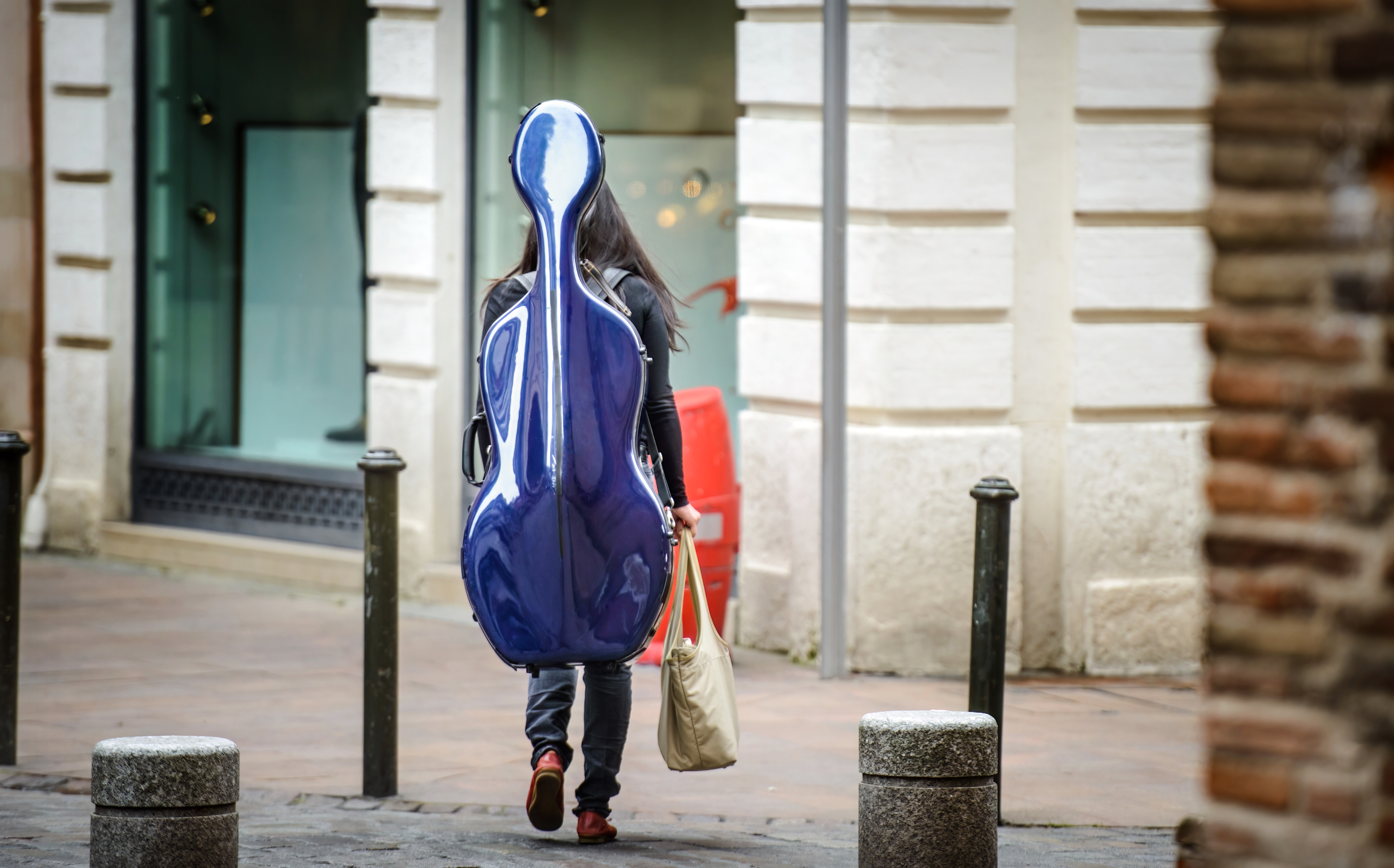 Musikerin trägt einen blauen Cellokasten im Straßenraum